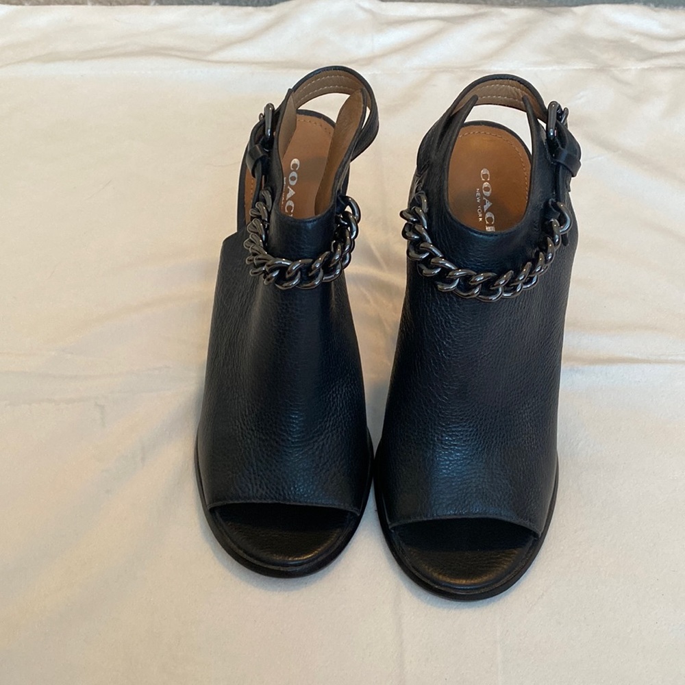 Open-toe Coach black leather mules with block heel and chain accent.